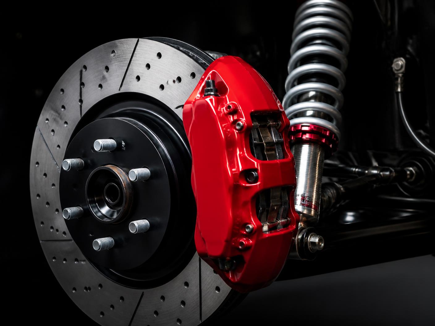 Performance brake rotor with red caliper beside coilover suspension shocks